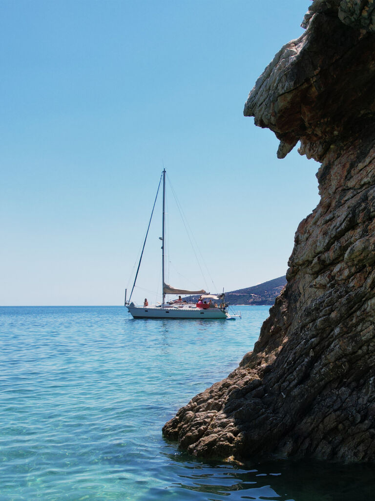 Sailing boat anchored in clear turquoise water beside a rocky shore